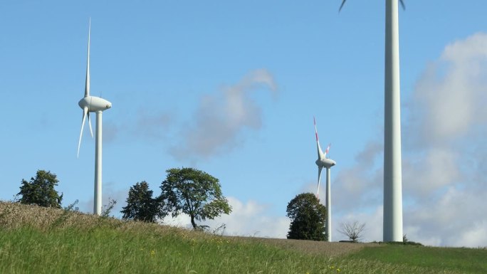 haarbr<e:1> ck风电场的三台风力涡轮机坐落在一片绿草如茵、蓝天白云的乡村风光中。