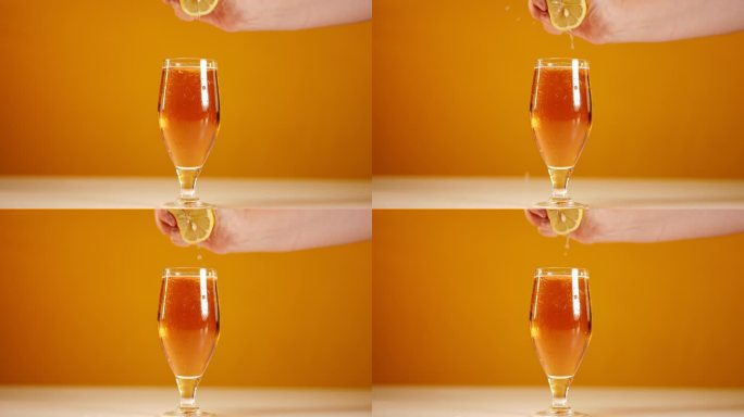 用手挤压柠檬片，用慢动作将柠檬汁倒入啤酒中。特写:无法辨认的白人男子在橙色背景下为清爽的酒精饮料调味