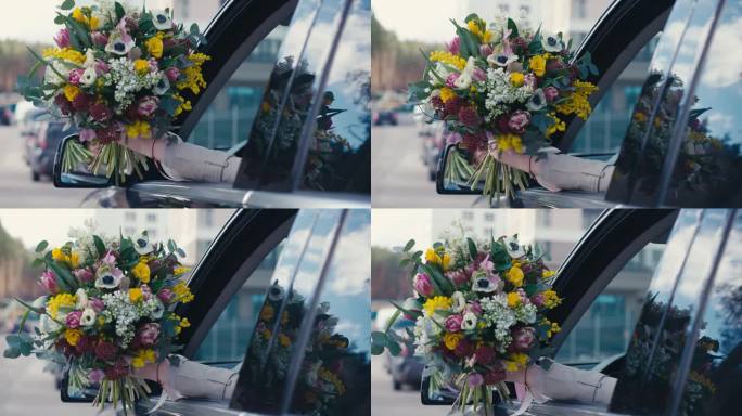 近景:一位女士的手从窗外伸出花束。无法辨认的白人年轻女子带着花在市区的车里。