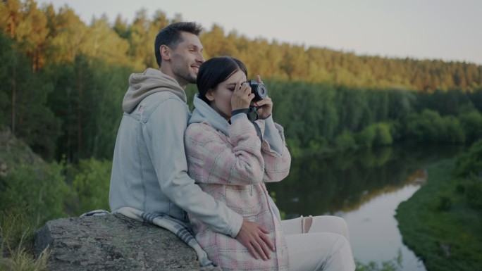 在国家公园，一对幸福的夫妇拿着相机观看美丽的风景，绿色的山林和河流