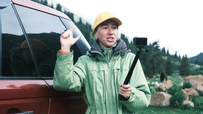 一位兴高采烈的女游客站在车旁边，正在拍摄她在天山自驾游的视频