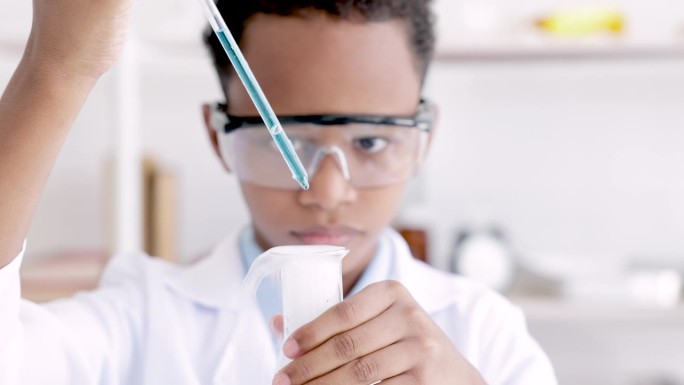 小学生在小学科学课上做化学实验时，戴着防护眼镜，穿着实验服，用挤压管从烧瓶中挤出水，分析和混合玻璃中