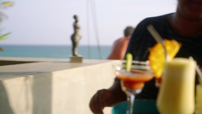 海景餐厅的女服务员把鸡尾酒放在托盘上。一位女士从海边酒吧的柜台上拿起装有热带酒精饮料的玻璃杯，并把它