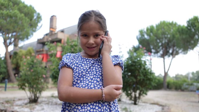 黑头发的女孩穿着蓝色印花裙子，在街上讲手机。童年、电话、科技、互联网、短信、幸福、度假、生活方式概念