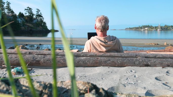 一位老人在海滩上用笔记本电脑休息