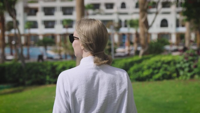 一个年轻女子正在一个豪华的度假胜地享受她的假期。这是一个阳光明媚的日子，棕榈树和令人印象深刻的高档酒