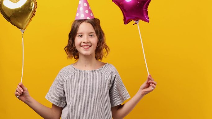 快乐，积极的十岁生日女孩戴着派对帽和气球