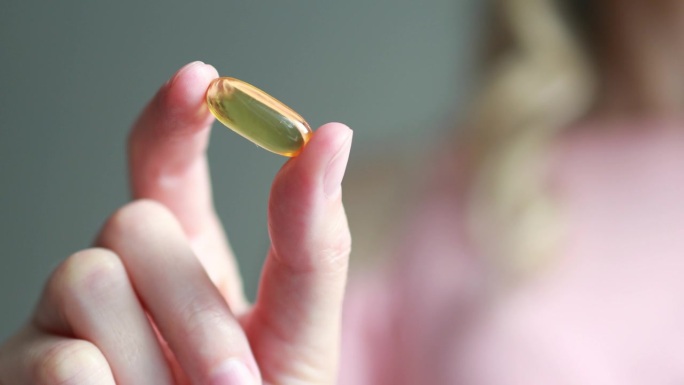 一个女人手掌里的黄色omega-3营养补充品或鱼油或维生素D3胶囊的特写
