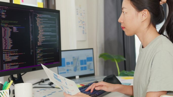 专业的年轻亚洲女孩的侧视图IT开发程序员在键盘上打字编码编程在电脑和笔记本电脑上的桌子上固定数据代码
