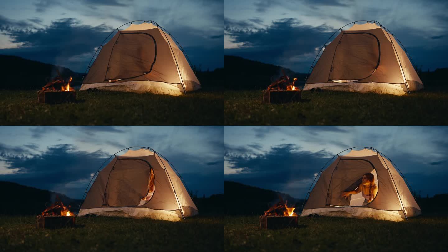 一个女人拉开帐篷门的拉链，凝视着外面附近的篝火