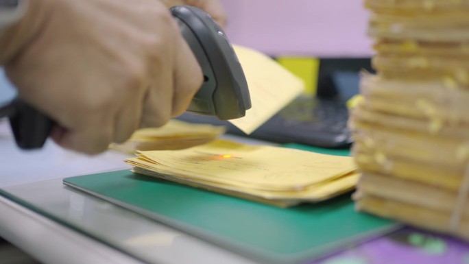 近距离人手用条码扫描器扫描黄色明信片上的条码，将数据信息转换成数字计算机。