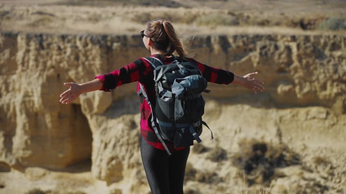 无忧无虑的女旅行者举起双臂站在悬崖上，欣赏峡谷的岩石景观