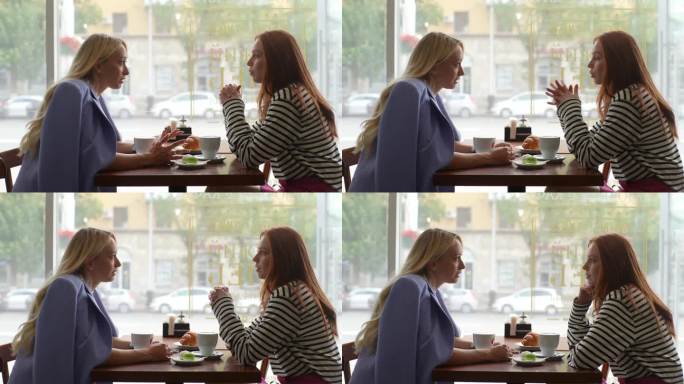 年轻的红发女人和金发的女性朋友聊天的侧视图，在舒适的餐厅一起喝茶，坐在桌子旁