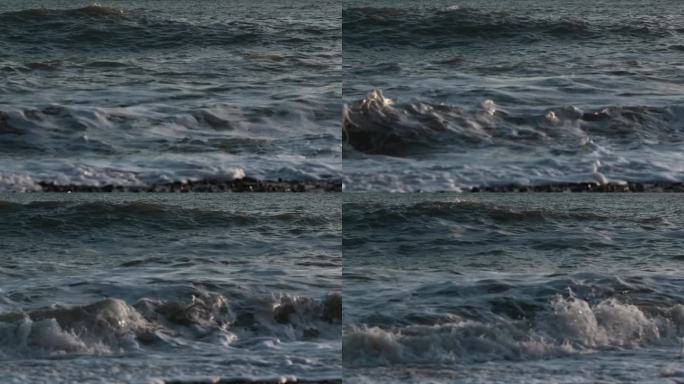 海上慢浪的特写。有创造力。美丽的波浪在石头岸边的慢动作。日落时美丽的海浪的石滩
