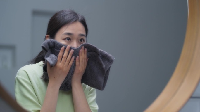 美丽的韩国女性在家里的浴室里洗脸。年轻女子享受早晨的美容程序，在一夜睡眠后恢复精神，用柔软的毛巾擦干
