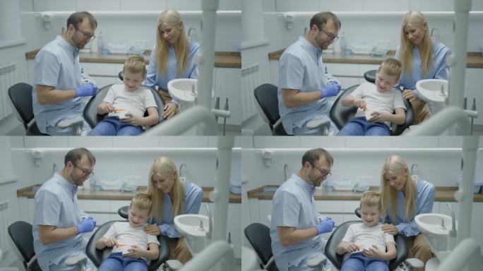 男牙医向男孩和他的妈妈展示下颌模型，教他们如何以有趣的方式正确刷牙。孩子坐在牙科椅上拍着手。慢动作