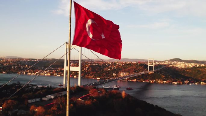 土耳其国旗迎风飘扬，背景是横跨博斯普鲁斯海峡和伊斯坦布尔的大桥