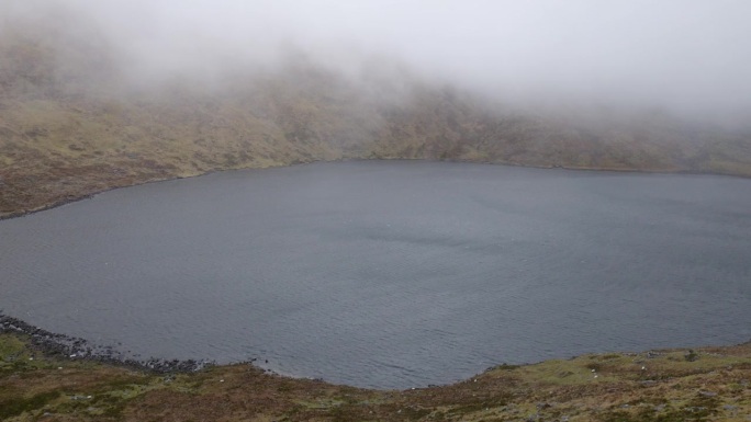 在爱尔兰刮大风的一天，一个宁静的高原湖泊的表面点缀着低空飞舞的云，描绘了一幅迷人的画面。