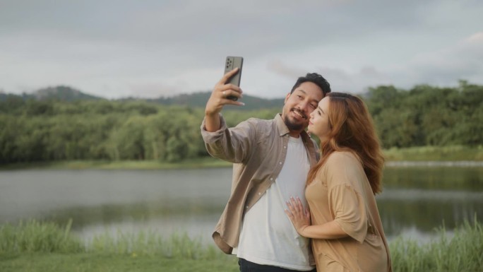 幸福的亚洲夫妇在湖边散步，用智能手机自拍度假。