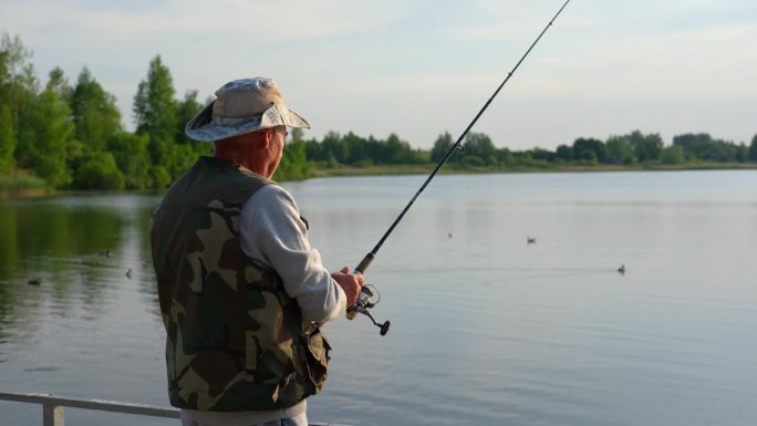 老人钓鱼。夕阳西下，一位白发苍苍的老渔夫从码头上抛下一缕丝线。积极的老年男性在湖中垂钓，旋转卷轴杆。