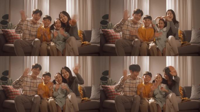 一个幸福的韩国家庭在家里的客厅里，微笑着对着镜头挥手。更换屏幕与家人和朋友的视频通话。友好的人的暖心