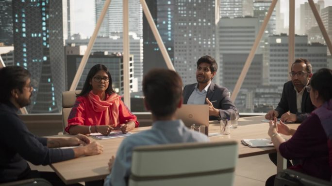 年轻的印度商人与才华横溢的经理团队进行对话。在现代办公大楼的会议室里，坐在会议桌后面的南亚同事