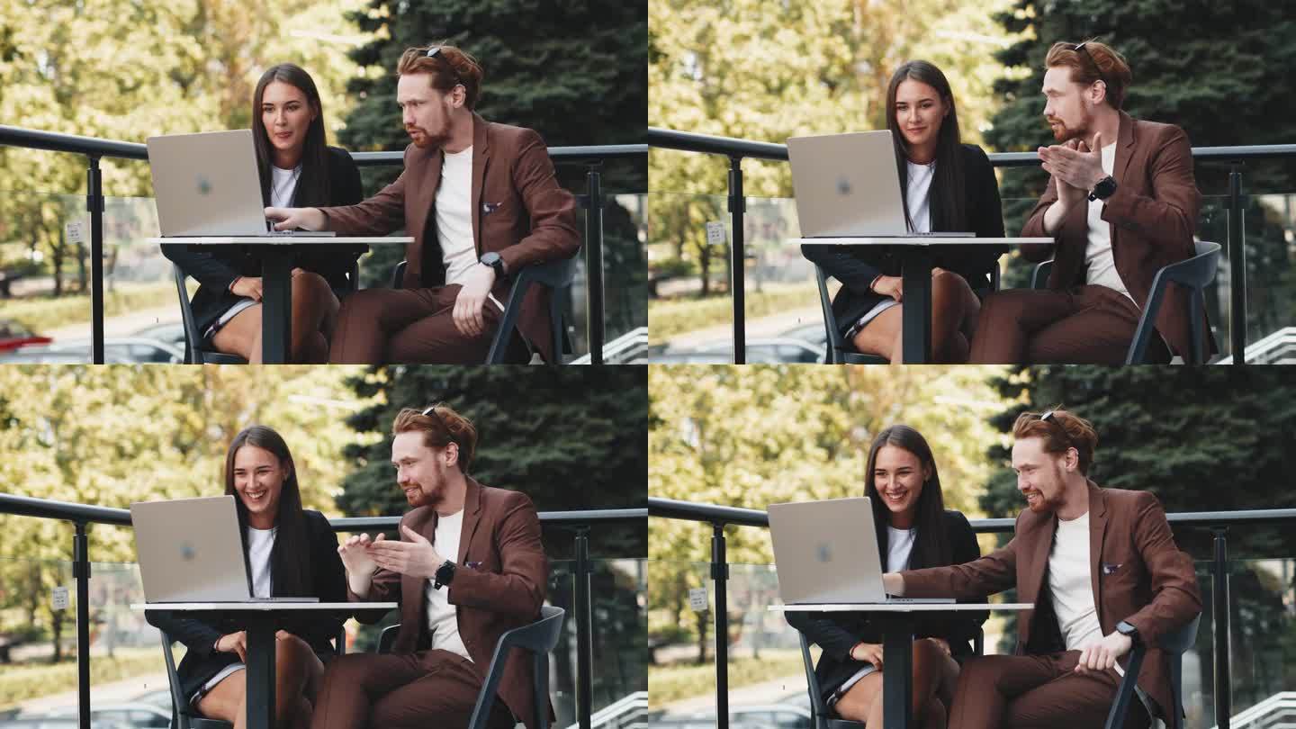一个女商人和一个商人在夏日露台上一起使用笔记本电脑的照片。商务人士高兴地庆祝一份重要合同的签订。