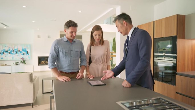 一名男性房地产经纪人向一对正在参观豪宅的已婚夫妇展示用平板电脑制作的小册子