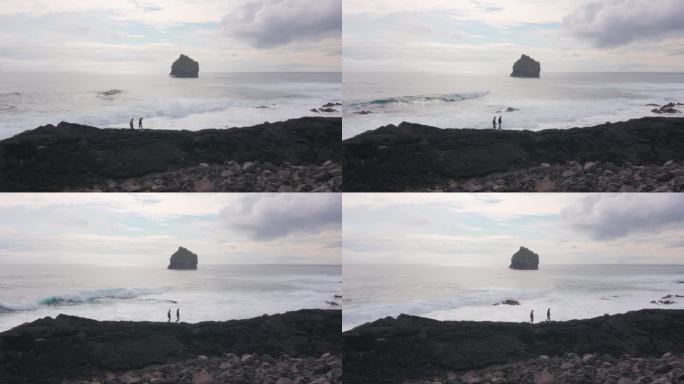 冰岛雷克雅那，两名男子走在岩石嶙峋的海岸线上，伴随着破碎的海浪