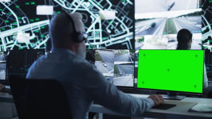 技术支持经理使用耳机和带有绿屏模拟显示的电脑。在一个黑暗的高科技监控室里，专注于一个电话和电脑工作
