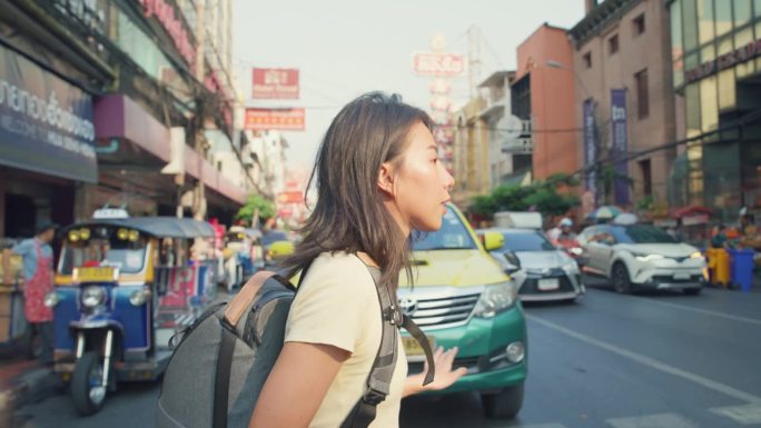 年轻的亚洲女背包客在城市街道上使用手机。假日度假旅行概念。
