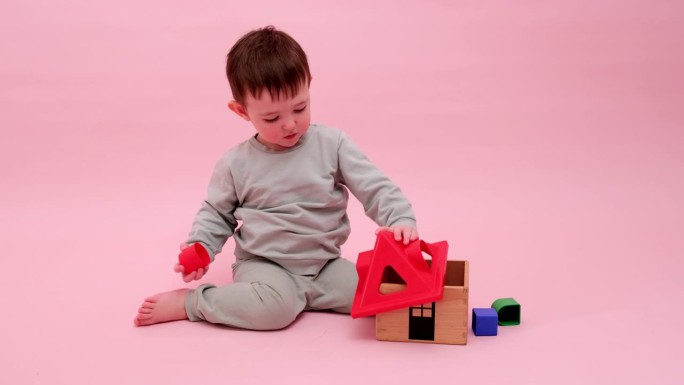 快乐的蹒跚学步的婴儿在工作室粉红色的背景上玩几何形状的分类器。小男孩玩益智玩具。孩子一岁八个月，身高