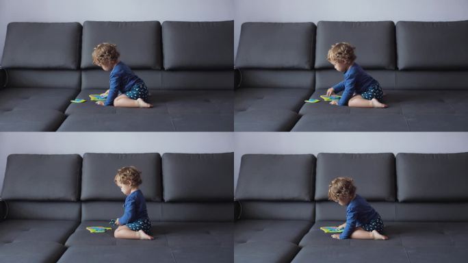 一个浅卷发的小女孩正坐在家里的沙发上，玩着学解大象图片的彩色拼图。