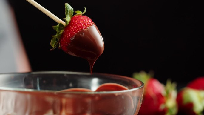 融化巧克力中的草莓特写，融化巧克力棒做火锅。把浆果放进巧克力慕斯。专业厨师烹饪蛋糕甜点。