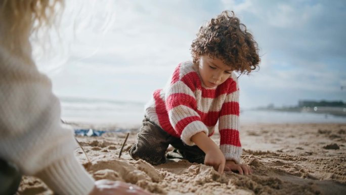 可爱的男孩在海边堆沙雕。专注的卷毛孩子在户外休息