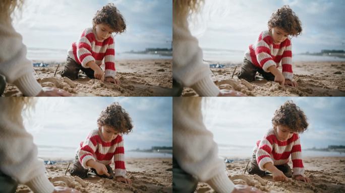 可爱的男孩在海边堆沙雕。专注的卷毛孩子在户外休息