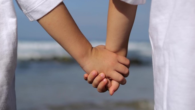 情绪平静，安抚孩子的手在海边的镜头。两个小孩子手牵着手，站在海边。近距离拍摄6-10岁儿童的手，他们