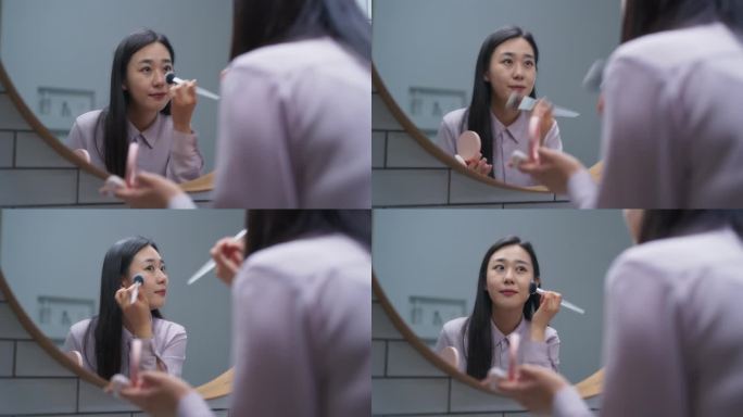 时髦的韩国女性用软毛刷在家里的浴室里涂色调粉底霜。美丽的女人照镜子，在脸上涂上天然的有机化妆品