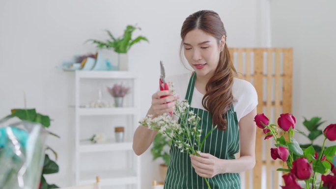 美丽的亚洲女花店花店工作与鲜花。一名女子开了一家花店，她剪花，制作花束，然后卖给顾客。花店的概念