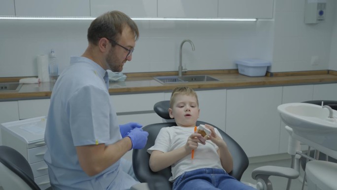 男牙医在会诊时教小男孩如何正确刷牙。男孩在人工颌上训练刷牙。慢动作