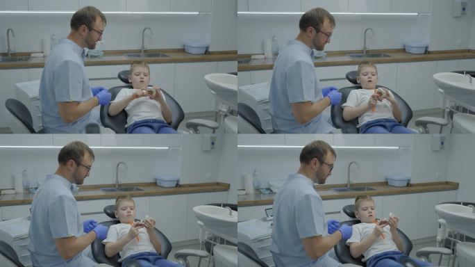 男牙医在会诊时教小男孩如何正确刷牙。男孩在人工颌上训练刷牙。慢动作