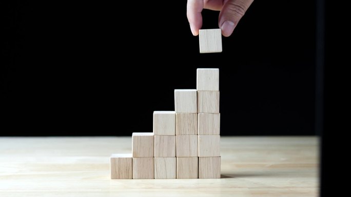 商人用手把木块堆成阶梯状，象征着生意的发展和壮大。业务发展，财务规划，投资和战略的概念化