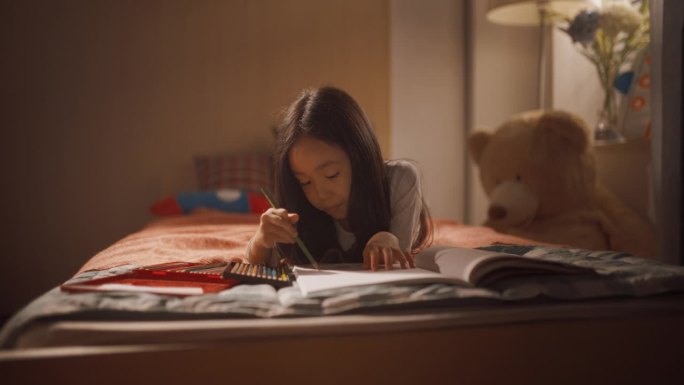 一个韩国小女孩躺在家里儿童卧室的床上用彩色铅笔在笔记本上画画的肖像。可爱的亚洲孩子在她舒适的房间里玩