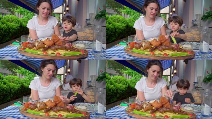 母亲和孩子在餐馆的餐桌上吃着丰盛的希腊餐盘，人们吃着丰盛的大餐