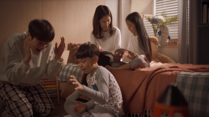 快乐的韩国家庭在儿童房一起玩耍。母女读童话故事，父子用积木搭太空站。放大在多莉广角镜头