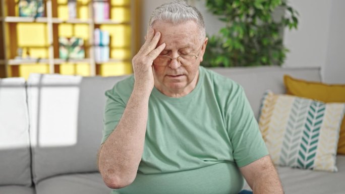 头发花白的中年男子坐在家里的沙发上患头痛