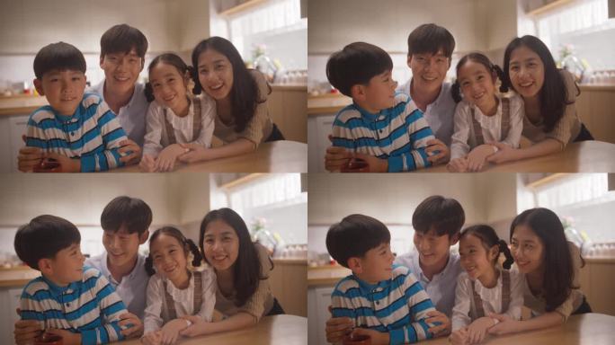 幸福的韩国家庭在阳光明媚的公寓里对着镜头微笑。年轻的父母和两个可爱的孩子摆姿势拍照，保留回忆，表达爱