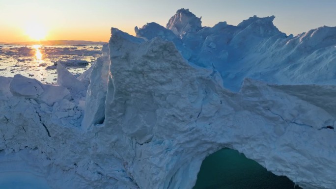 落日的鸟瞰图穿透冰山的边缘。日落时的冰山和冰洞。冰川融化，全球变暖，北极自然景观