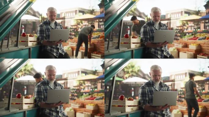 中年商人在笔记本电脑上工作，联系农场供应商关于新鲜农产品的周日市场活动。一名男子坐在街头小贩的摊位旁