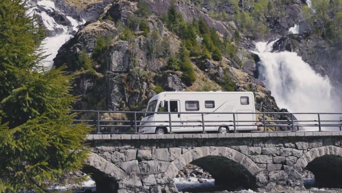 露营车行驶在挪威瀑布边的老桥上